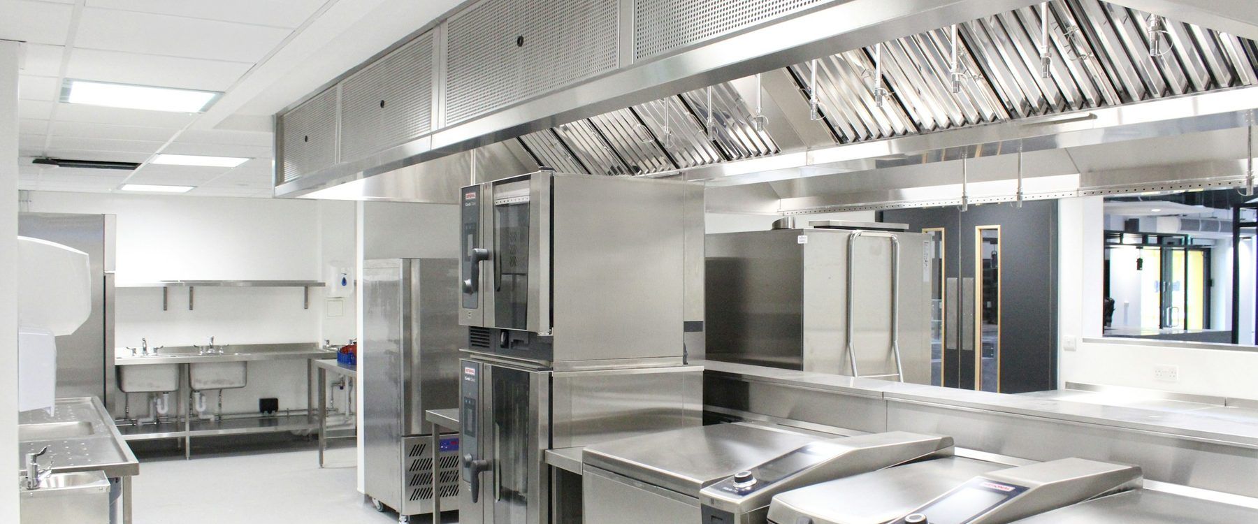 Stainless commercial kitchen exhaust hood with baffle grease filters and fire-suppression nozzles over cooking equipment