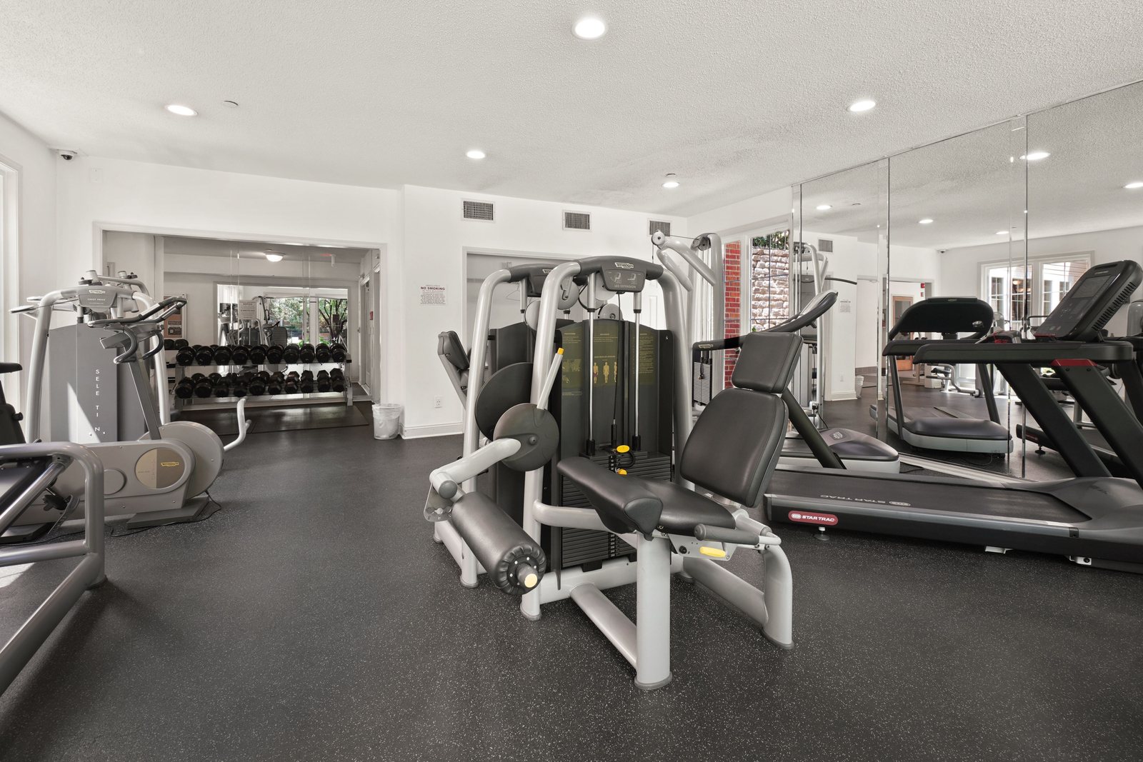 Fitness center floor with cardio machines, selectorized equipment and a dumbbell rack on rubber flooring
